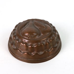 May include: A vintage copper mold for making pear-shaped desserts. The mold has a fluted edge and a detailed pear design on the top.