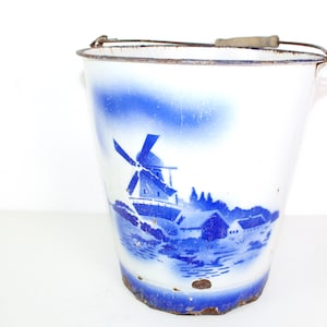 May include: White enamel bucket with a blue and white windmill scene painted on the side. The bucket has a metal handle with a wooden grip.