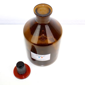 Puede incluir: Una botella de vidrio marr&oacute;n con una tapa negra y una etiqueta blanca que dice "&Aacute;CIDO CLORH&Iacute;DRICO 37%".