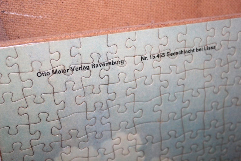 K&ouml;nnte beinhalten: Ein blaues Puzzle mit dem Text "Otto Maier Verlag Ravensburg Nr. 15.455 Seeschlacht bei Lissa" darauf gedruckt.