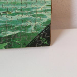 K&ouml;nnte beinhalten: Nahaufnahme der Ecke einer Puzzlebox mit einem gr&uuml;nen und blauen Bild von Wasser. Die Box ist mit "Ravensburger Spiele" beschriftet.