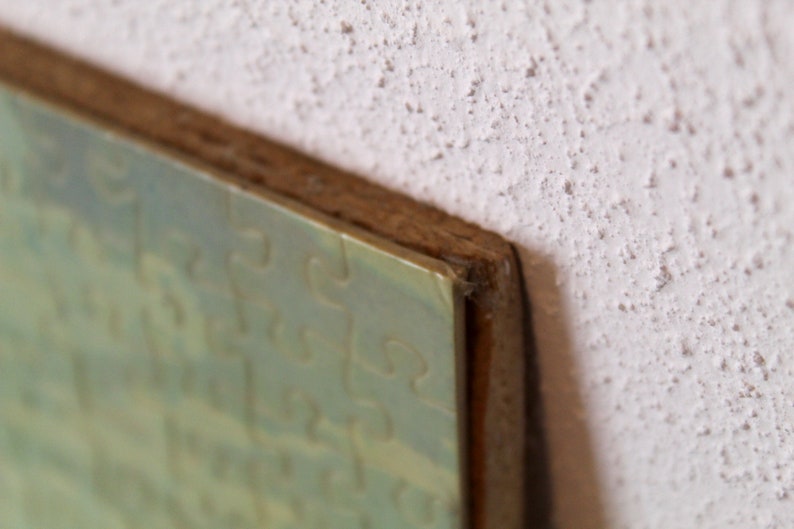 K&ouml;nnte beinhalten: Nahaufnahme eines gerahmten Kunstwerks mit einem abstrakten Design in Gr&uuml;n und Blau. Der Rahmen ist aus Holz und hat eine hellbraune Oberfl&auml;che.