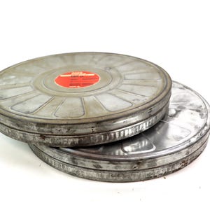 Peut inclure: Deux bobines de film métalliques vintage avec une étiquette rouge sur la bobine du dessus. Les bobines sont empilées l'une sur l'autre.