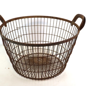 Puede incluir: Una cesta de alambre de metal grande y oxidada con dos asas. La cesta es redonda y tiene un diseño de malla de alambre.