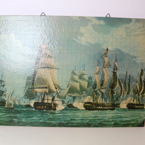 K&ouml;nnte beinhalten: Ein Vintage-Puzzle, das eine Seeschlacht mit mehreren Segelschiffen zeigt, die Kanonen aufeinander feuern. Die Schiffe sind detailliert mit wei&szlig;en Segeln und braunen R&uuml;mpfen dargestellt, vor einem blauen Himmel mit wei&szlig;en Wolken. Das Meer ist tief blaugr&uuml;n.