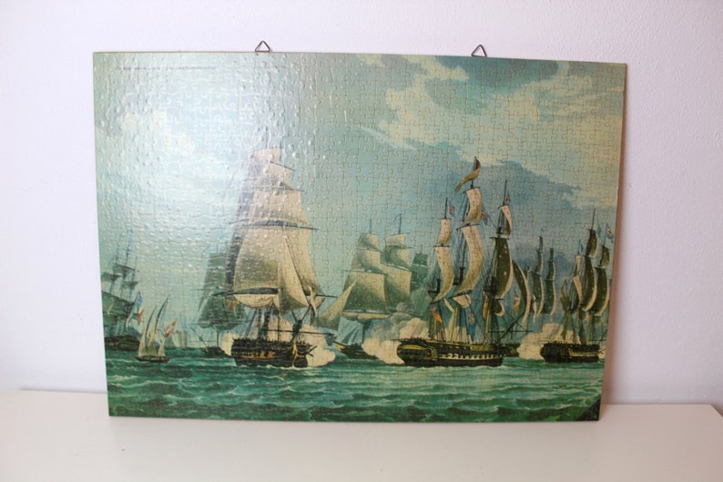 K&ouml;nnte beinhalten: Ein Vintage-Puzzle, das eine Seeschlacht mit mehreren Segelschiffen zeigt, die Kanonen aufeinander feuern. Die Schiffe sind detailliert mit wei&szlig;en Segeln und braunen R&uuml;mpfen dargestellt, vor einem blauen Himmel mit wei&szlig;en Wolken. Das Meer ist tief blaugr&uuml;n.