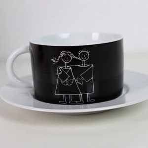 May include: A black and white teacup and saucer set featuring a simple illustration of two stick figures holding hands. The figures are outlined in white against a black background.