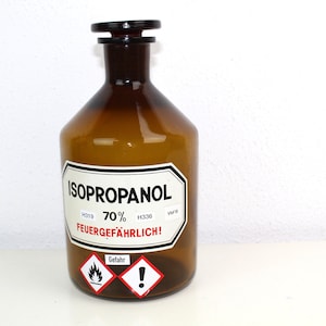 Puede incluir: Una botella de vidrio marr&oacute;n con una etiqueta blanca que dice "ISOPROPANOL 70% FEUERGEF&Auml;HRLICH!" con un s&iacute;mbolo de advertencia rojo y blanco. La botella tiene una tapa de pl&aacute;stico negro.
