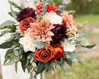 May include: A bridal bouquet with a mix of burgundy, peach, and white flowers, accented with greenery.