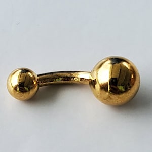 May include: A gold-colored belly button ring with two round balls.