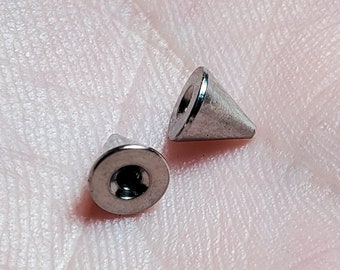 Op de afbeelding: Twee zilveren, kegelvormige lichaamssieraden. Eén stuk is een platte basis met een schroefdop. Het andere stuk is een kegel met een afgeronde punt.
