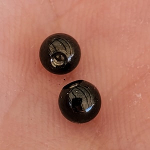 May include: Two black round beads with a small hole in the center.