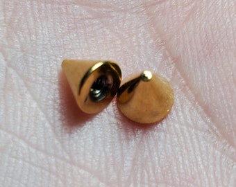 Op de afbeelding: Twee goudkleurige metalen kegels, een met een schroefdraadgat, voor gebruik als piercing.