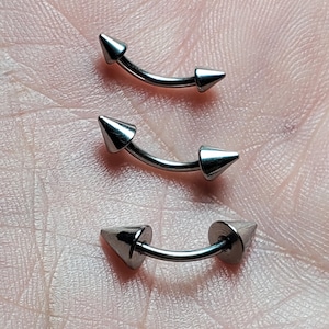 May include: Three silver curved barbell body piercings with pointed ends. The piercings are different sizes.