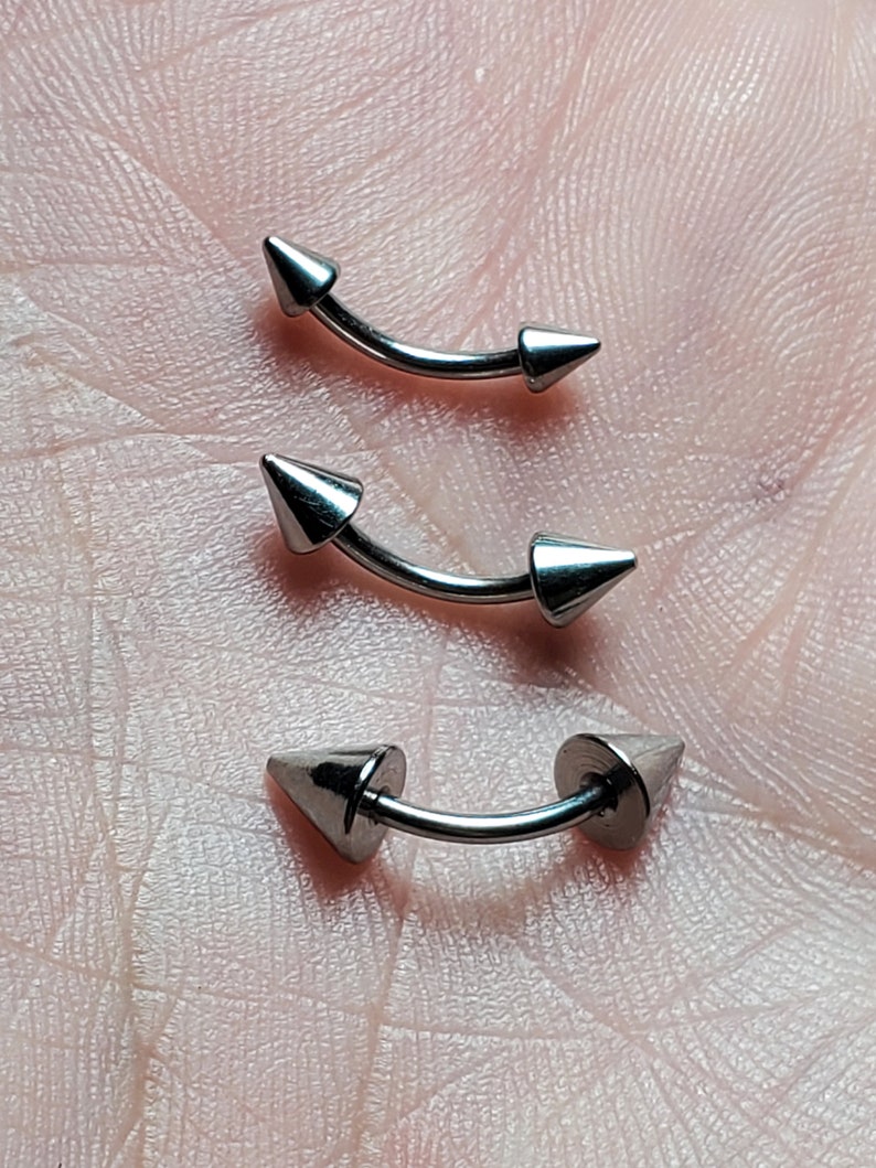 May include: Three silver curved barbell body piercings with pointed ends. The piercings are different sizes.
