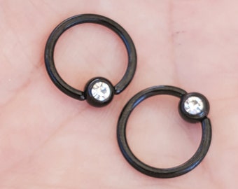 Op de afbeelding: Twee zwarte ronde ringen met een heldere strasssteen in het midden van elke ring.