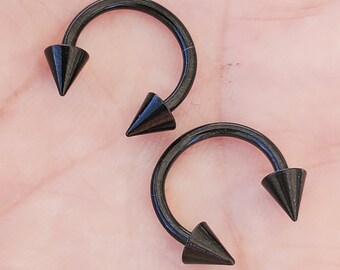 Op de afbeelding: Twee zwarte ronde barbell piercings met puntige uiteinden.
