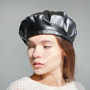May include: A black leather beret with a smooth, shiny finish. The beret is worn on a person's head.
