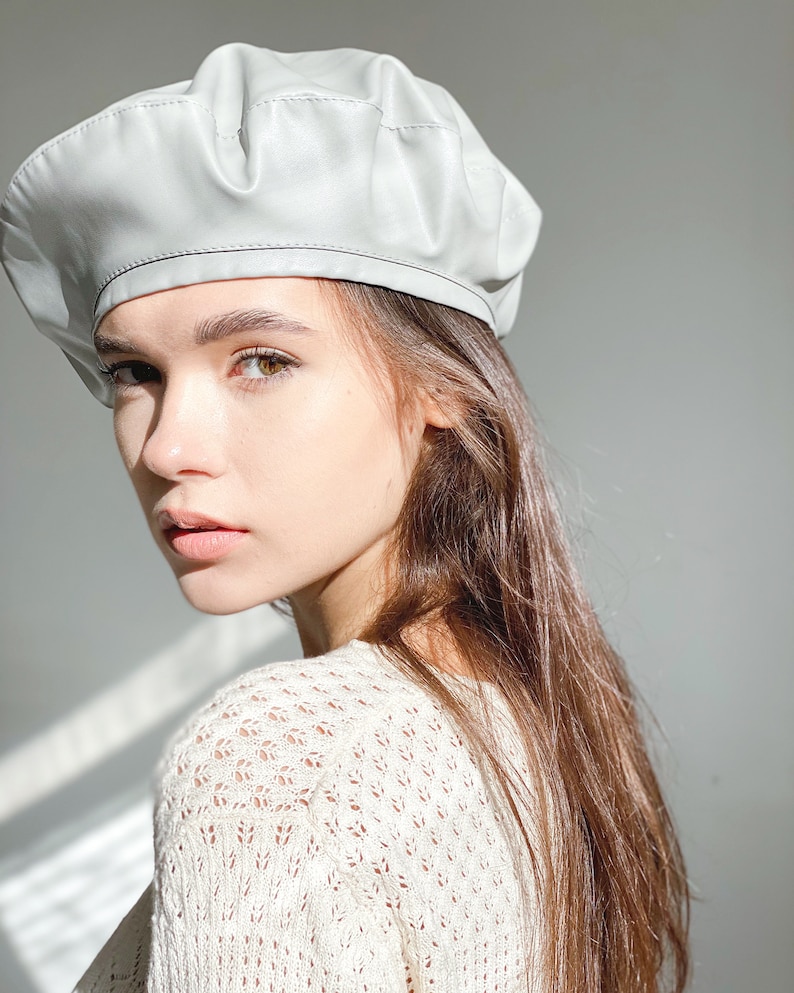 May include: A light gray beret made of faux leather. The beret has a slightly wrinkled texture and a simple design.