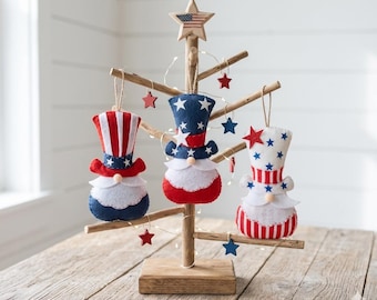 Könnte beinhalten: Ein dekorativer Baum aus Holz mit drei Zwergornamenten in Rot, Weiß und Blau. Die Ornamente sind wie Uncle Sam-Hüte und -Körper geformt. Der Baum ist mit einem Holzstern gekrönt und hat kleine rote Sternornamente.