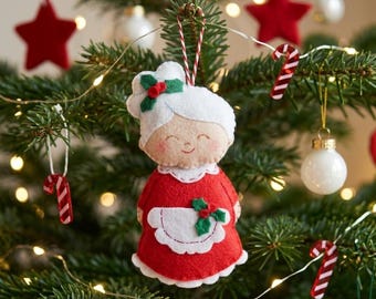Könnte beinhalten: Ein Weihnachtsbaumschmuck aus Filz in Form von Mrs. Claus, mit rotem Kleid und weißer Schürze. Der Schmuck hat ein lächelndes Gesicht und ist mit Stechpalmen verziert. Weitere Ornamente sind rote Sterne, Zuckerstangen und weiße Kugeln.
