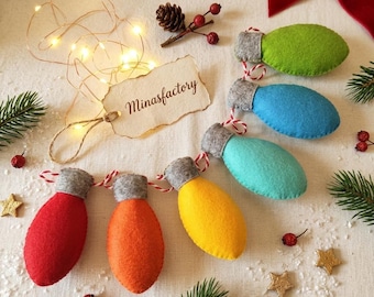Könnte beinhalten: Eine Lichterkette aus bunten Weihnachtsbaumschmuck-Lichtern aus Filz in Rot, Orange, Gelb, Türkis, Blau und Grün. Jede Leuchte hat eine graue Kappe und eine rot-weiß gestreifte Schnur. Das Bild enthält ein Etikett mit "Minasfactory".