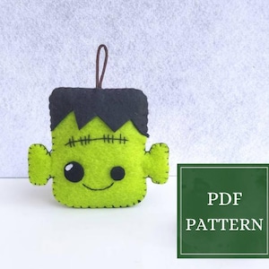 May include: A handmade green felt Frankenstein's monster ornament with black hair and stitched details. The ornament has a smiling face and a brown loop for hanging. A green square with the text "PDF PATTERN" is on the right.