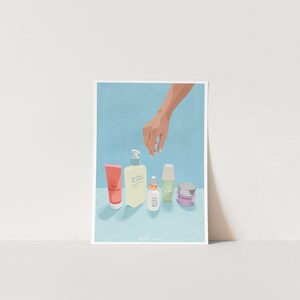 May include: A hand reaches towards a collection of five skincare products on a light blue background. The products include a pink tube labeled "Love Yourself", a yellow bottle labeled "Be Kind To Others", a green bottle labeled "Give Your Skin Some Love", a green tube labeled "The Daily", and a purple jar labeled "Be Grateful".