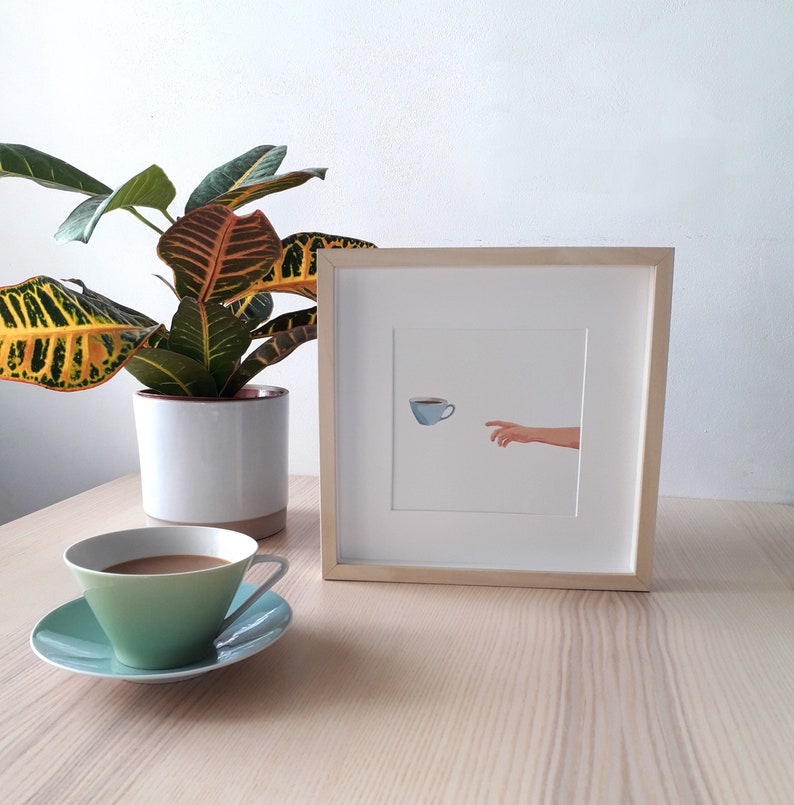 Puede incluir: Una ilustraci&oacute;n enmarcada de una mano que se extiende hacia una taza de caf&eacute; azul. La ilustraci&oacute;n est&aacute; sobre un fondo blanco y est&aacute; enmarcada en un marco de madera clara.