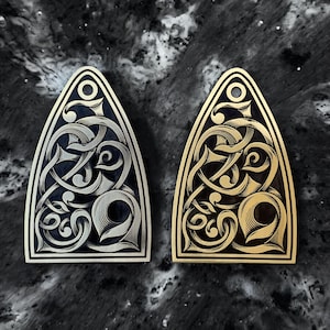 May include: Two guitar pickguards with intricate, ornate designs. One is silver with a black background, and the other is gold with a black background.