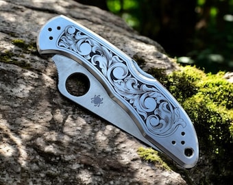 Spyderco Delica con cachas de acero inoxidable y grabados ornamentales.