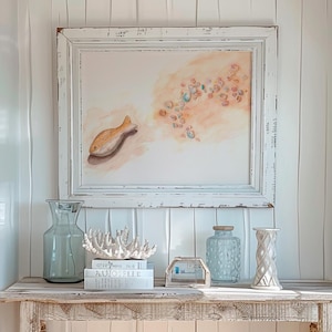 Peut inclure: Une console en bois blanchi à l'aspect rustique, ornée d'objets décoratifs. Au-dessus, une peinture à l'aquarelle encadrée d'un poisson et de coraux. Vases en verre et décor corallien.