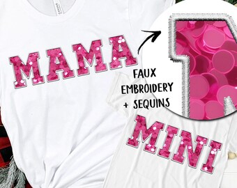 May include: White t-shirts with the words "MAMA" and "MINI" in pink sequined letters. The design includes faux embroidery and sequins. The shirts are displayed with holiday decorations.