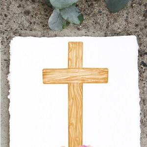 May include: A watercolor illustration of a wooden cross with pink and peach flowers at the base. The cross is a light brown color and has a wood grain texture. The flowers are arranged in a cluster and have green leaves.