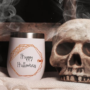 May include: White stainless steel tumbler with a gold geometric frame and a spider web design. The text "Happy Halloween" is written in black inside the frame. A small orange spider is in the corner of the frame.