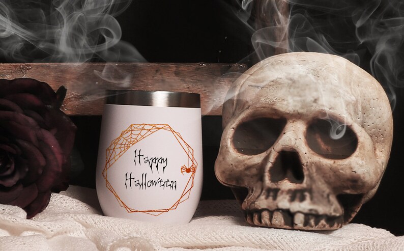 May include: White stainless steel tumbler with a gold geometric frame and a spider web design. The text "Happy Halloween" is written in black inside the frame. A small orange spider is in the corner of the frame.