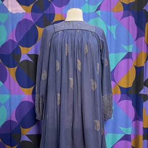 Puede incluir: Un vestido azul marino con estampado paisley dorado. El vestido tiene mangas largas y un escote fruncido.