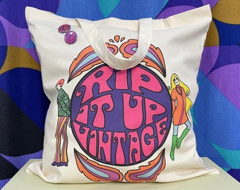 May include: A white canvas tote bag with a pink circle and the text "Rip It Up Vintage" in purple and pink letters. Two figures are on either side of the circle, one in green and yellow and the other in orange and green.