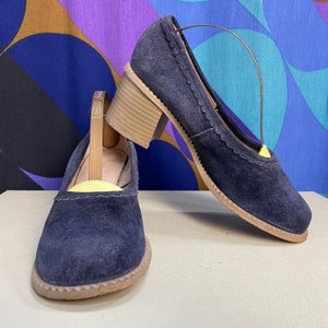 May include: A pair of navy blue suede heeled shoes with a scalloped edge and a wooden heel.