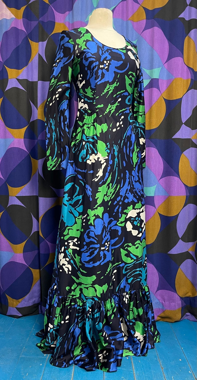 May include: A long-sleeved maxi dress with a black background and a colorful abstract floral print in shades of blue, green, and white. The dress has a ruffled hem.