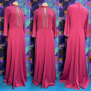 May include: A long, magenta maxi dress with a high neckline and long sleeves. The dress is adorned with a silver beaded design down the front.