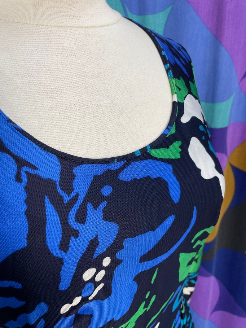 May include: A sleeveless dress with a scoop neck and a blue, green, and white abstract print on a navy background.