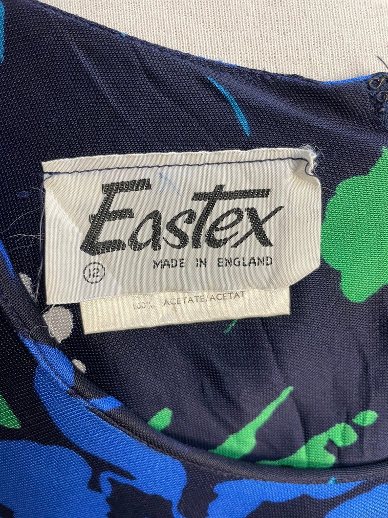 May include: A navy blue dress with a green, blue, and white abstract print. The dress has a label that reads "Eastex Made in England 100% Acetate/Acetat"