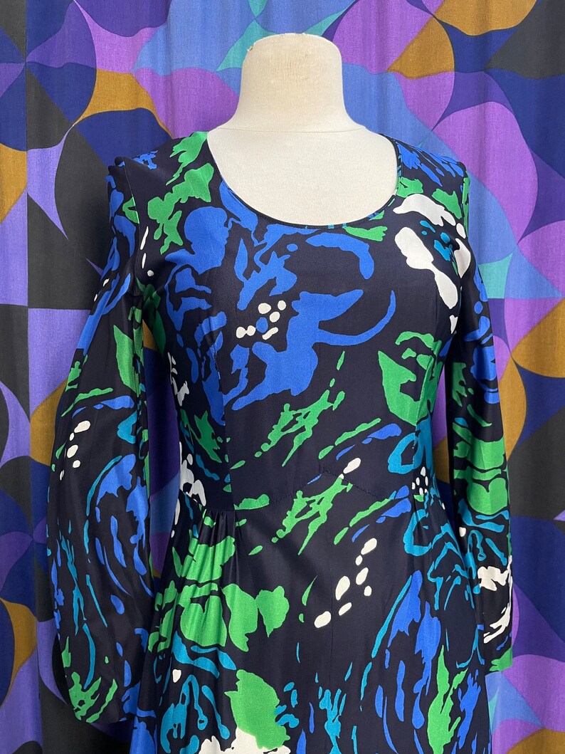 May include: A long-sleeved dress with a blue, green, and white abstract floral print. The dress has a round neckline and a fitted bodice.