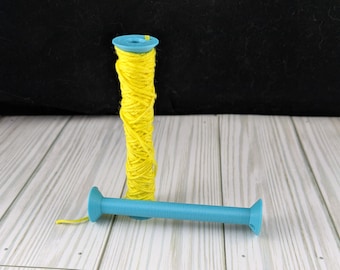 May include: A spool of yellow thread wound around a blue plastic bobbin. The bobbin has a small hole in the top and a larger hole on the side.