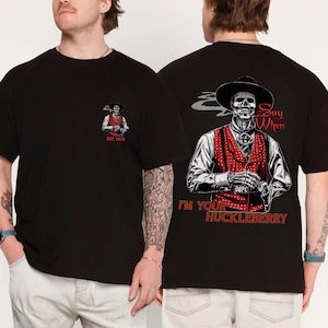 May include: A black t-shirt featuring a graphic of a skeleton wearing a cowboy hat and a red polka-dot vest. The back print includes the text Say When and I'M YOUR HUCKLEBERRY. The front chest area displays a smaller version of the same graphic.