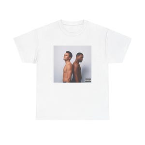 Puede incluir: Camiseta blanca con una imagen cuadrada de dos hombres sin camisa de espaldas. La imagen tiene un fondo neutro y una etiqueta de advertencia para padres en la esquina inferior derecha. La camiseta está hecha de un material suave y cómodo.