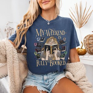 Pu&ograve; includere: T-shirt blu navy con la scritta "My Weekend Is Fully Booked". La grafica presenta una donna che legge un libro circondata da altri libri. La maglietta &egrave; realizzata in un materiale morbido.