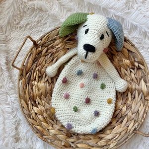 May include: A crocheted white dog toy with colorful polka dots and a black nose. The toy is sitting in a woven basket.