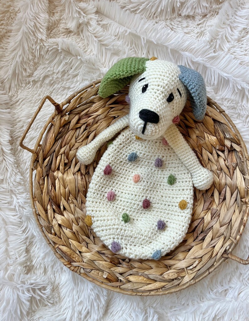 May include: A crocheted white dog toy with colorful polka dots and a black nose. The toy is sitting in a woven basket.